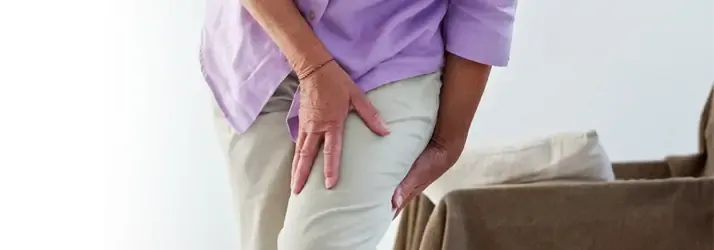 Person holding their thigh in pain while standing