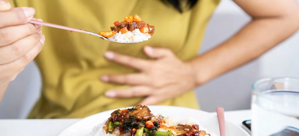 Woman clutching her abdomen with a spoonful of food in hand